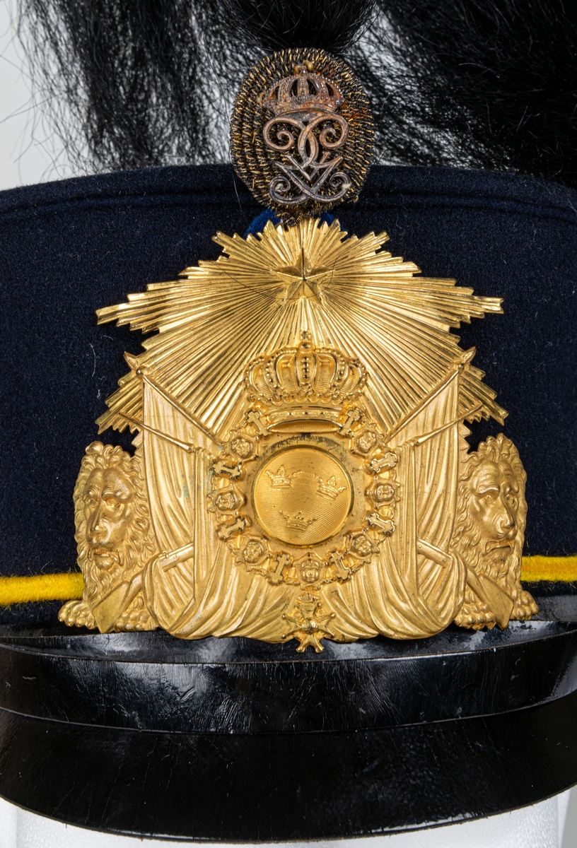 Mössa, uniformsmössa, blå med stor mässingsbricka, lilla riksvapnet omgivet av lejon, flaggor och med kungl. krona ovanför samt 5-uddig stjärna med strålar. Överst plymfäste med tagelplym. M/1899.