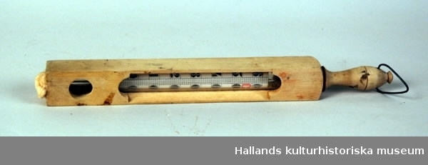 Badtermometer i träfodral med handtag. Termometer celsiusgraderad på papper från -7 C° - + 68 C°. Fodral av trä med öppningar på två långsidor. Svarvat handtag med krok. Öppen i den andra kortänden med stopp av bomullstuss.