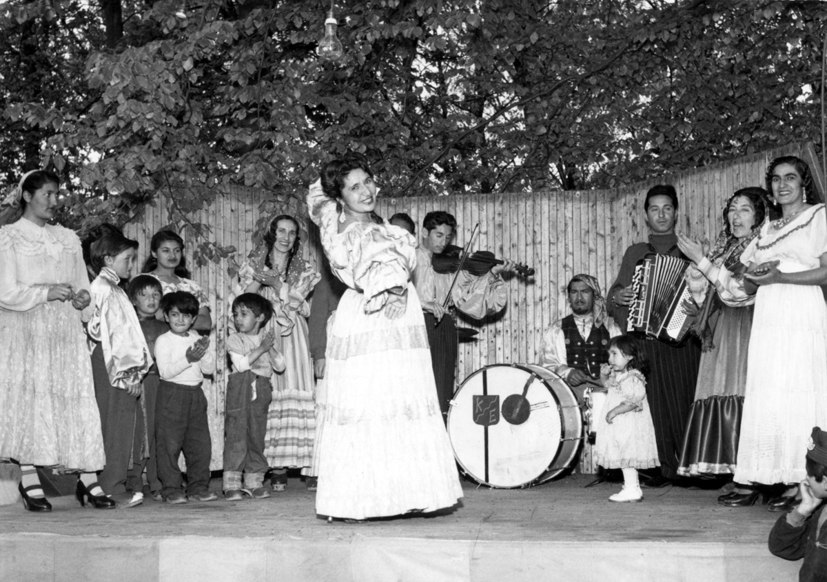 En kvinna uppträder med ungersk romsk dans i Folkets park i Lund 1954. Orkestern spelar csardas. Att vara musikant har historiskt varit ett vanligt yrke bland romer i Sverige.