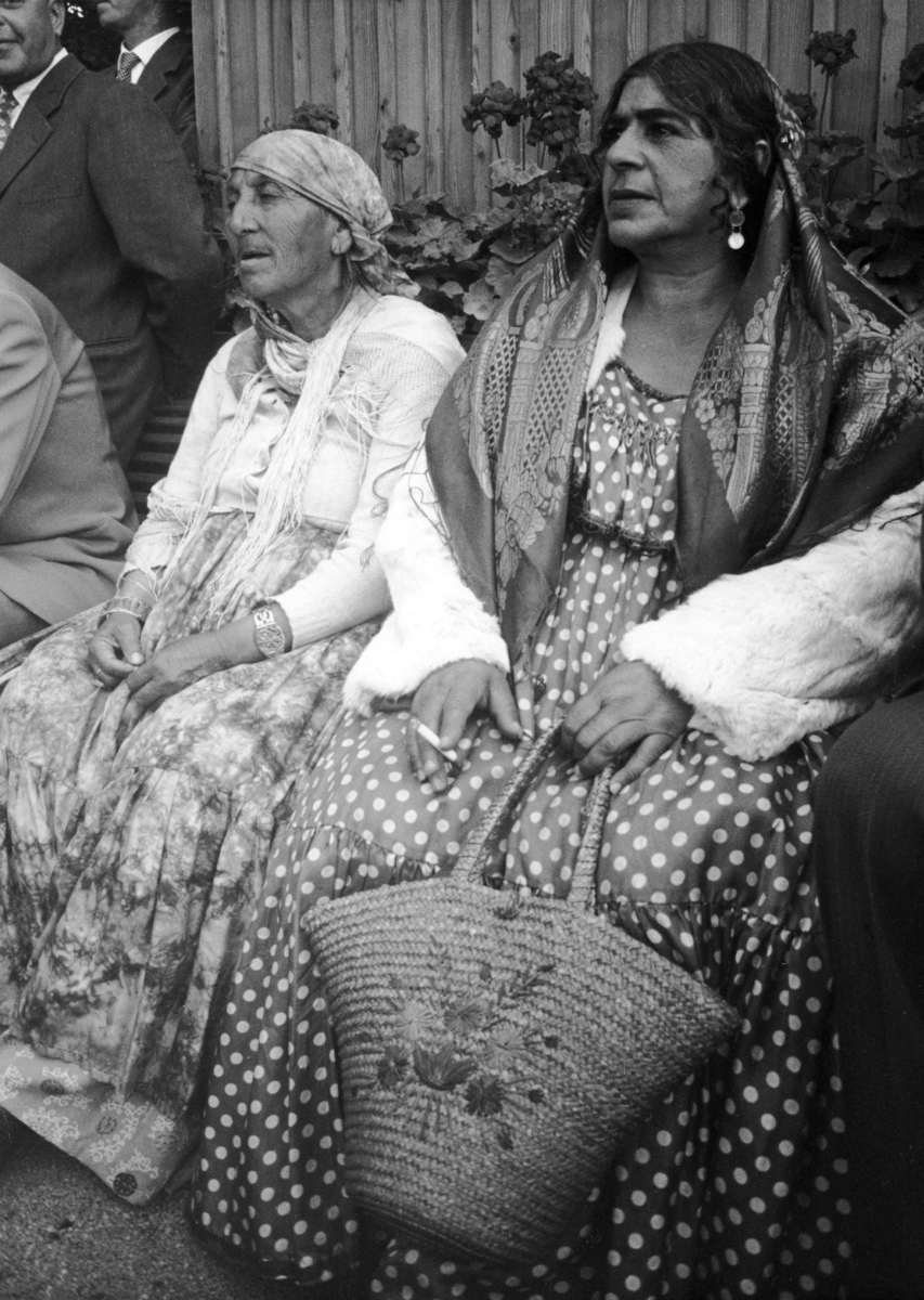 Två romska kvinnor sitter intill varandra på en bänk. En av kvinnorna bär en dikhlo.