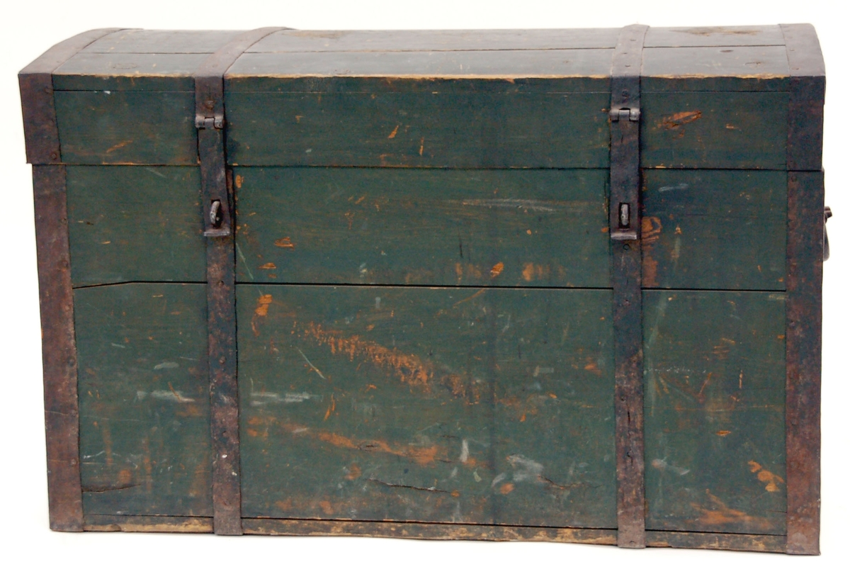 Kista av furu, mörkgrön målning, locket något bukigt. Järnbeslag på kanter samt vid låsöglor m.m.