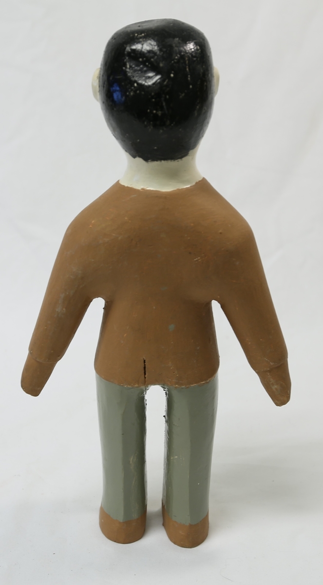 Malt med svart hår og Hitler-bart, beige ansikt og hals, brun skjorte og hansker, grå bukser og brune sko.