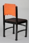 Sortmalt stol i furu med oransj ryggbrett. Ryggbrettet har lærimiterende bemaling og et blad/blomstermotiv skåret i relieff. Løst trapesformet sete med hestehårstrekk.