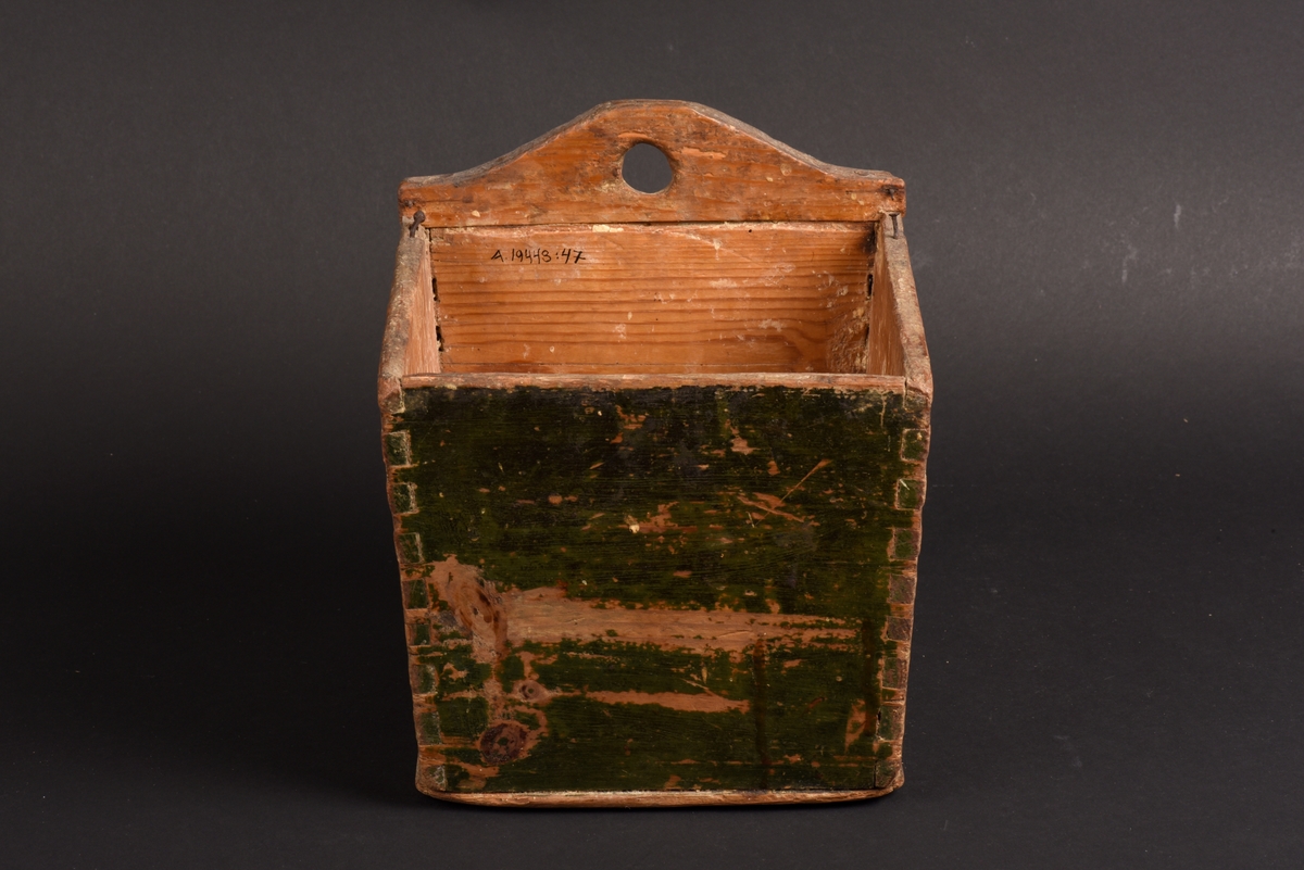 Kvadratisk låda av trä, troligen en låda för mjöl. Målad i mörkgrön färg på utsidan. Bakstycket är något högre och har en svängd kant, där ett hål för upphängning finns. Lock saknas.