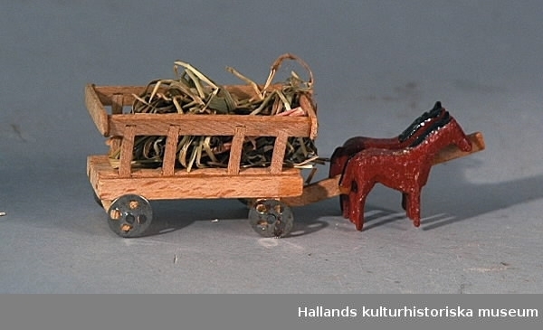Häst och vagn av trä. En skrinda med hö dragen av två bruna hästar.
