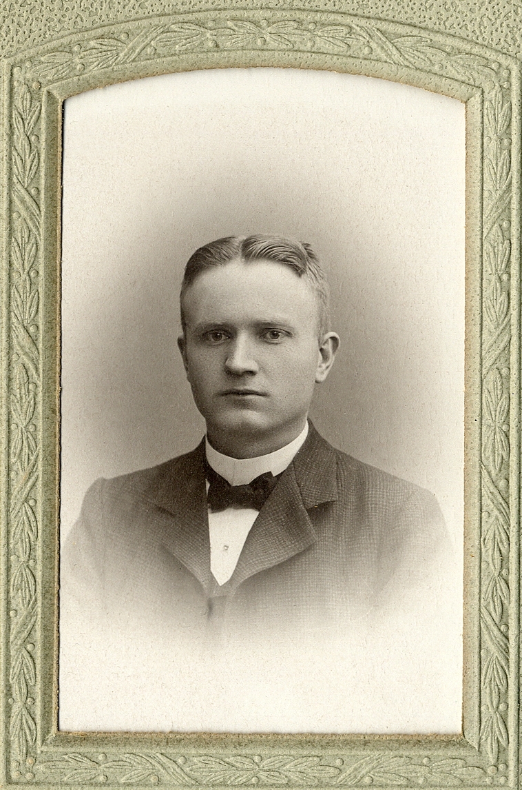 En okänd man, klädd i kavajkostym med stärkkrage och fluga. I nedre högra hörnet syns inpräglat årtal: "1905". 
Bröstbild, halvprofil/en face. Ateljéfoto.