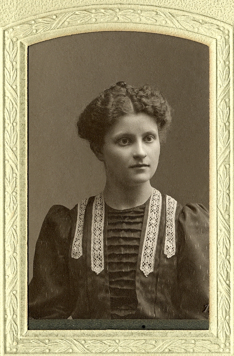 En okänd ung kvinna i mörk klänning med vita spetsbårder, I nedre högra hörnet syns inpräglat årtal: "1906". 
Bröstbild, halvprofil. Ateljéfoto.