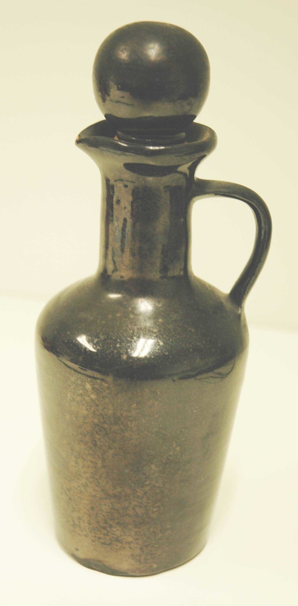 Svart keramikkflaske med kork. Korken har kule, også i keramikk.