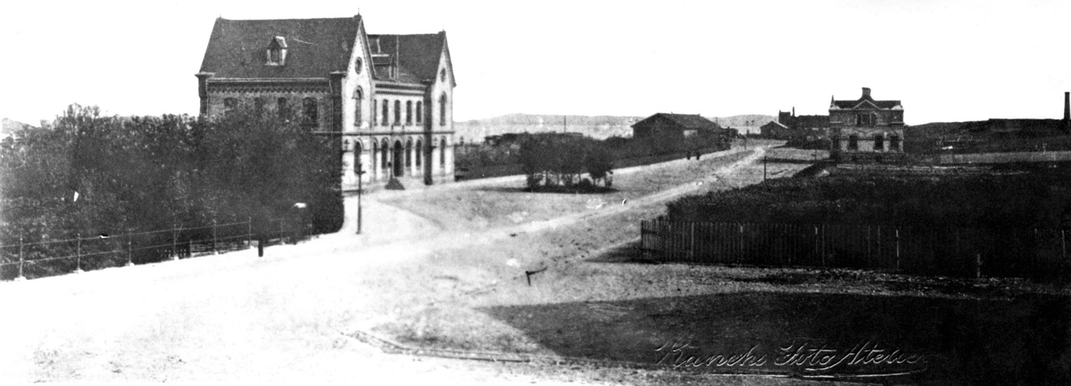 Järnvägsstationen i Varberg, ritad av ingenjör J. A. Tistrand för Varberg-Borås järnväg, invigd 1880. Västra Vallgatan fick förlängas när stationen anlades och bilden är tagen mot nordväst. Till höger syns den sk Uddenbergska villan vilken uppfördes på 1880-talet åt järnvägschefen.