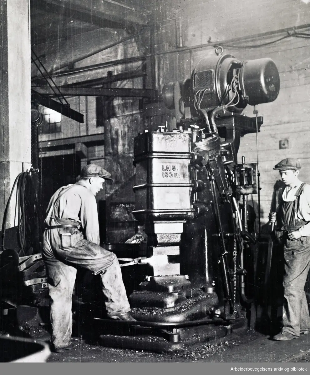 Smeder i arbeide med elektrisk drevet lufthammer på et mekanisk verksted i Sulitjelma, ca. 1925 - 1930.