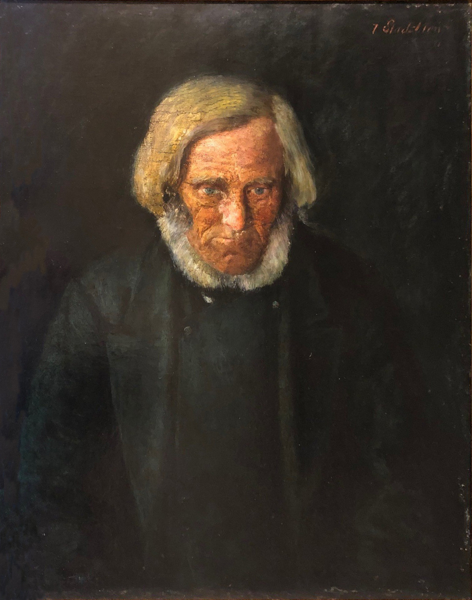 Portrett av eldre mann med grått hår, skjegg og mørke klær.  