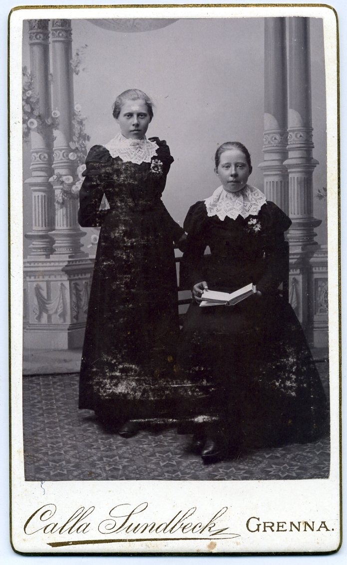 Kabinettsfotografi: gruppbild med två okänd ung kvinna, en stående och en sittande med en bok i knät. Bägge har en stor spetskrage..
