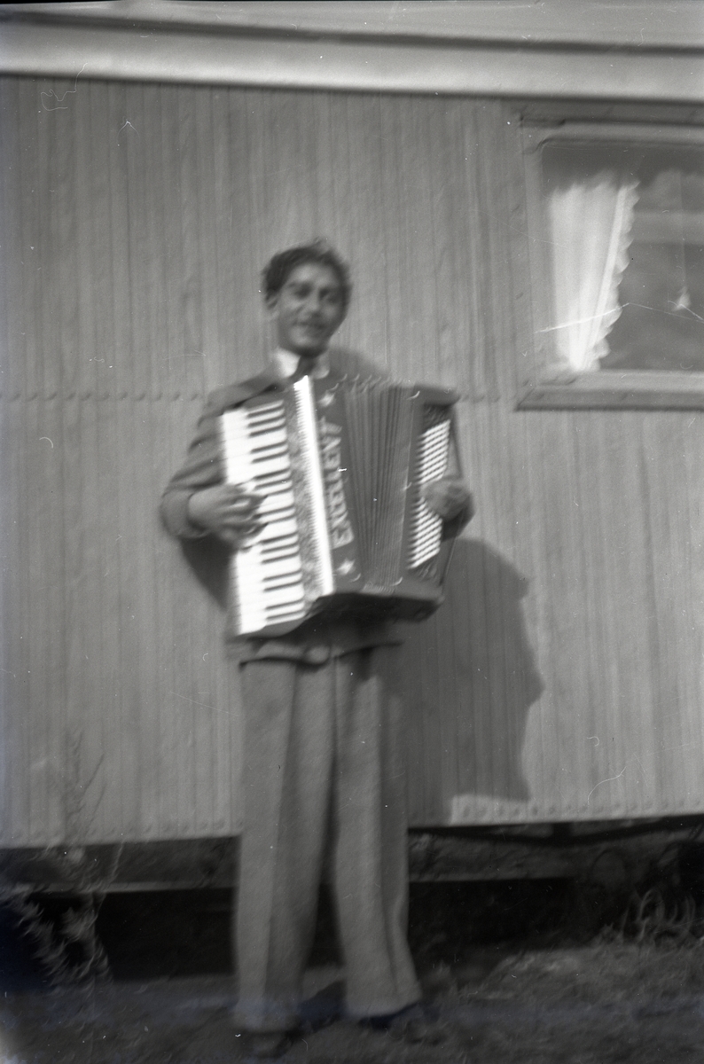 En ung man med ett dragspel poserar för kameran framför en bostadsvagn. Att vara musikant har historiskt varit ett vanligt yrke bland romer i Sverige. Musicerandet har ofta kombinerats med tivoliverksamhet, teater eller lustspel av olika slag. Dessa verksamheter mötte en kraftig nedgång i och med tevens genomslag under 1950- och 1960-talen.