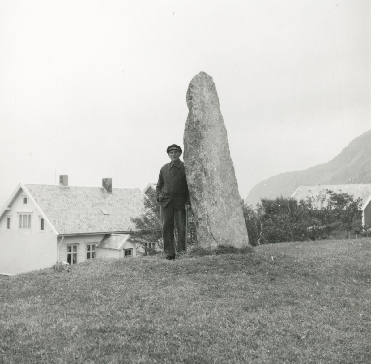 En mann står ved ein bautastein på Alnes, Godøy.