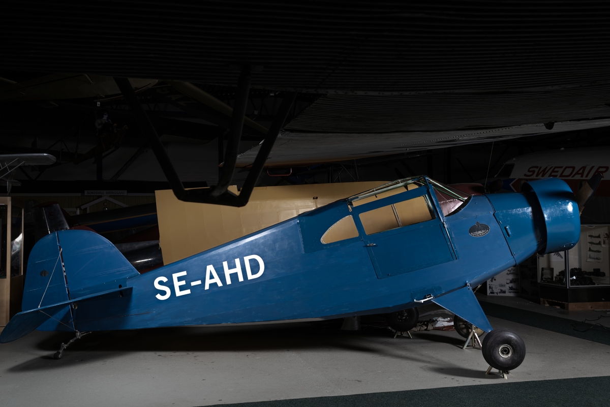 Flygplan av modell GV-38. Motorflygplan med täckt kabin och två sittplatser i tandem. Högvingat monoplan, blåmålat.
