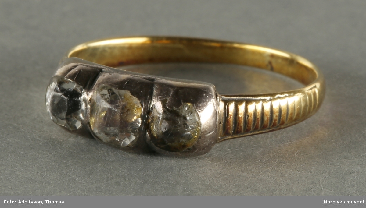 Fingerring med skena i gulmetall tvärgående räfflor. Ringen dekorerad med tre stycken bergkristaller infattade i vitmetall.

/Cecilia Wallquist 2019-03-11