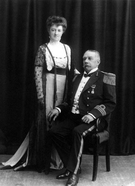 Gruppbild med en i militär uniform med orden sittande i en stol. En kvinna står intill honom. De är friherrinnan Maria von Rosen med maken kommendörkapten och friherre Robert von Rosen.