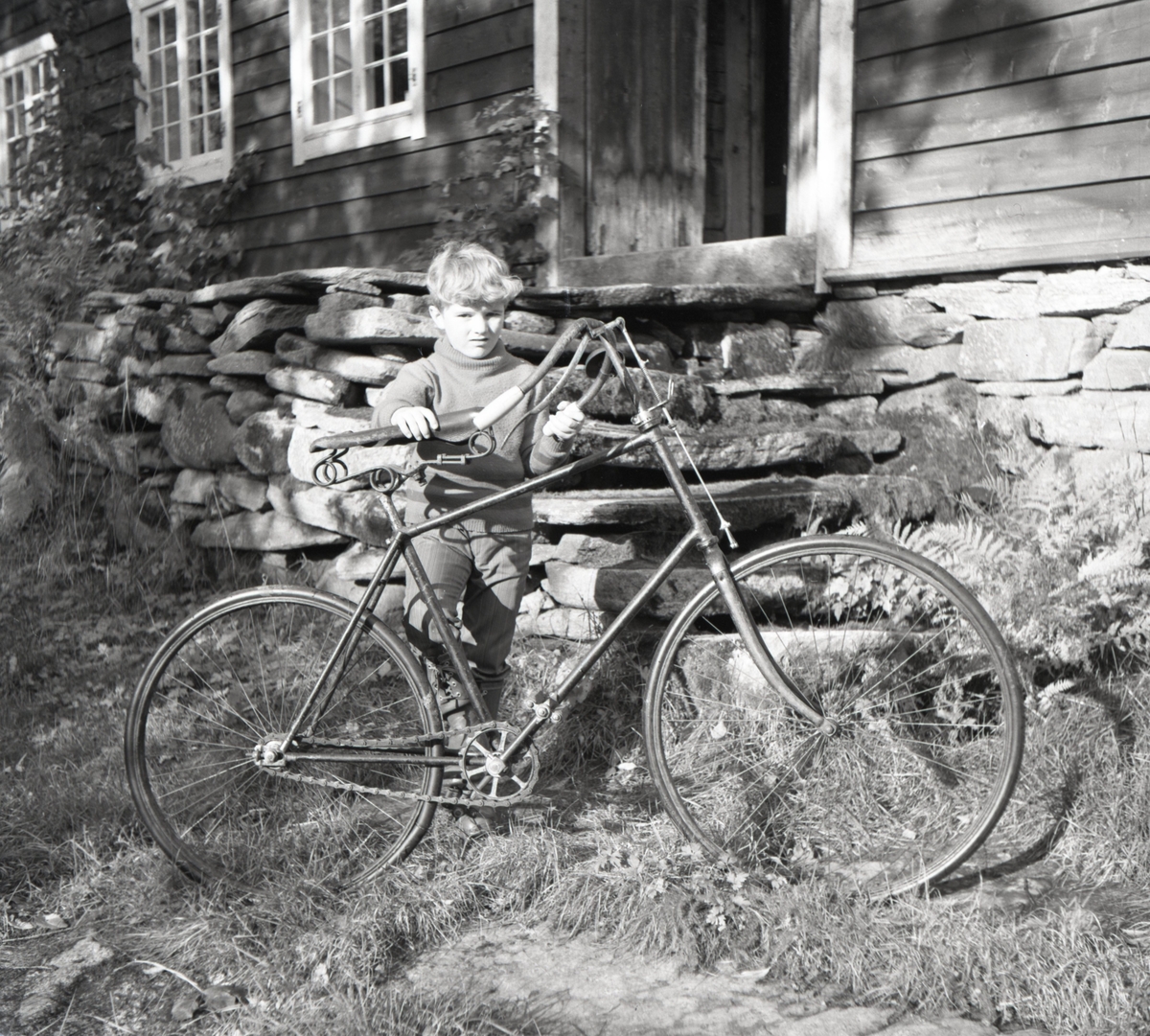 Motiv av en gutt med en gammel sykkel utenfor et hus.