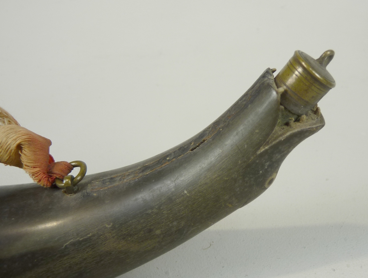 Kruthorn av mörkgrönt horn, i spetsen i form av ett ormhuvud. Metallöglor och ett rött bomullsband.