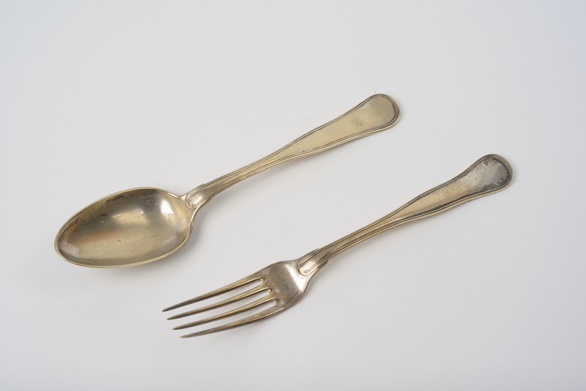 Skje og gaffel er heilstøpt i ei sølvlegering, utan spesielt mønster berre to opphøde liner i ytterkant i skaftet. 