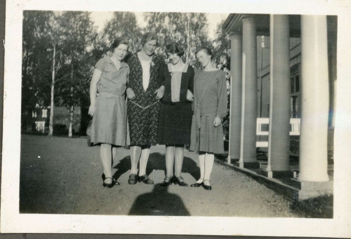 Elever fra husmorskolen på Skansgården, Kongsvinger, 1928. Fire unge kvinner i finklær foran hovedinngangen med søyler.