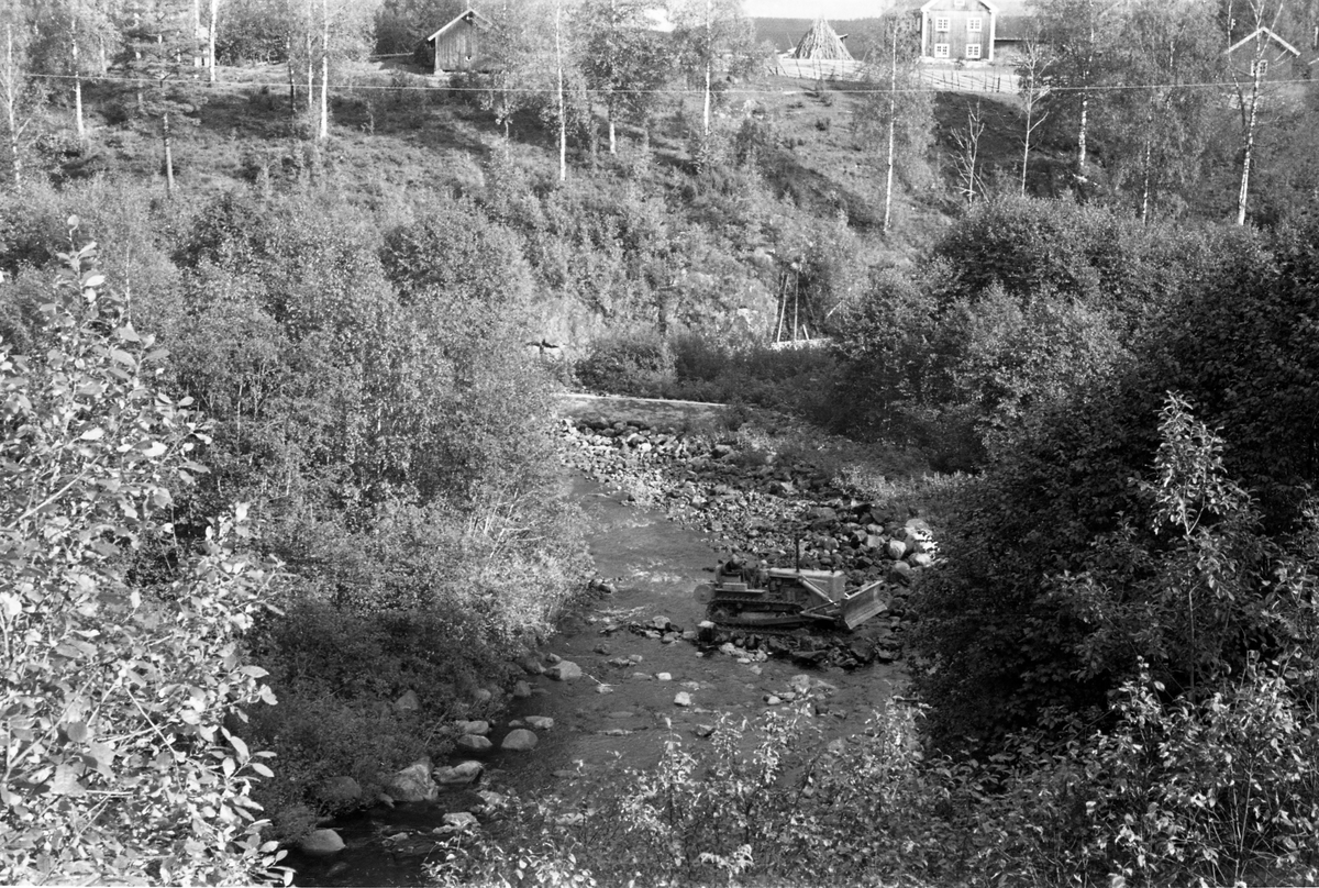Bulldoser av merket Caterpillar i aktivitet under Brattfossen i Løsetåa i Nord-Odal i Hedmark, fotografert i 1954. Brattfossen ligger nederst i dette vassdraget, like før Løsetåa forenes med Mørkåa, for å bli Kilåa, som etter cirka 500 meter renner ut i innsjøen Råsån eller Råsen. I 1950- og 60-åra tok Glomma fellesfløtingsforening i bruk slike maskiner for å drive «elverensnings- eller elveforbedringsarbeider». Dette dreide seg om å fjerne stein- og grusører fra elveløpene med sikte på å oppnå enklere og mer effektiv fløting. Her ble noe av steinen fra elvefaret skjøvet inn mot elvebredden ved hjelp av det frontmonterte skjæret på bulldoseren. Høsten 1954 meldte lokalavisene at Glomma fellesfløtingsforening ville få i stand en ny «fløterordning» som skulle halvere fløtingskostnadene i dette vassdraget. Bulldoserarbeidene var sikkert et viktig virkemiddel i bestrebelsene for å nå et slikt mål.
