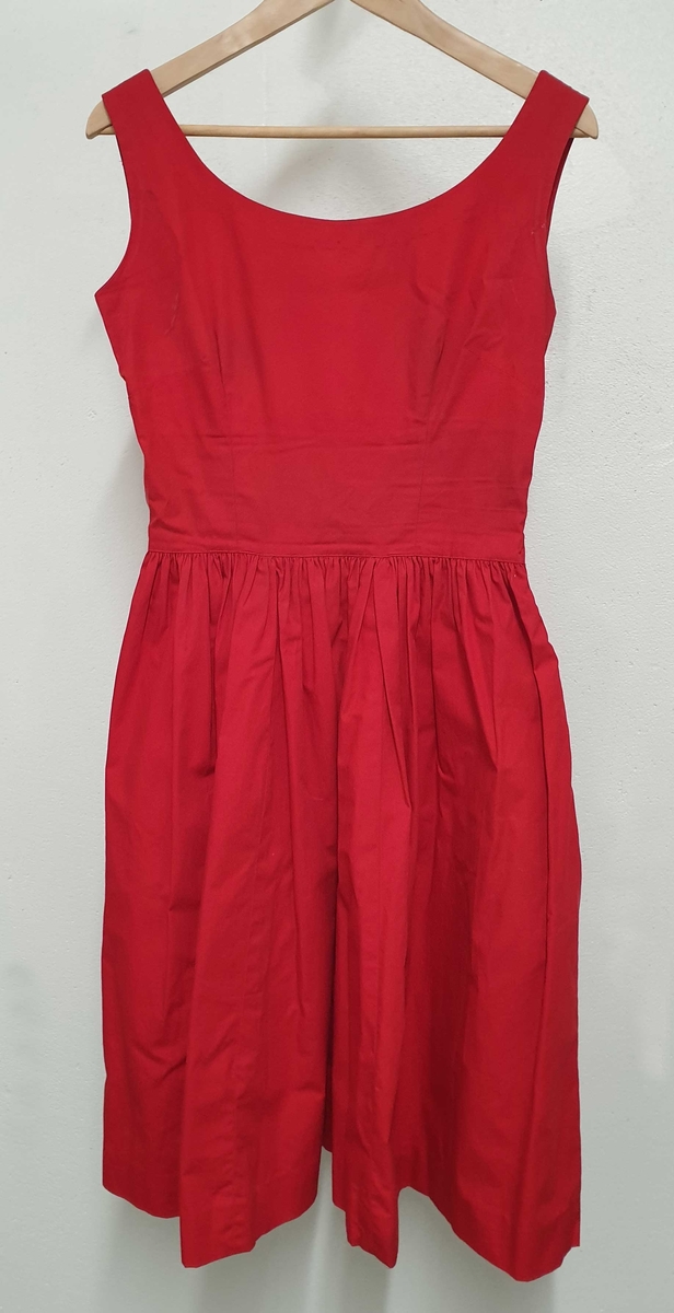 Rød ermeløs kjole med tilhørende rød jakke med halvlange ermer, hvite blondekanter og hvite knapper.