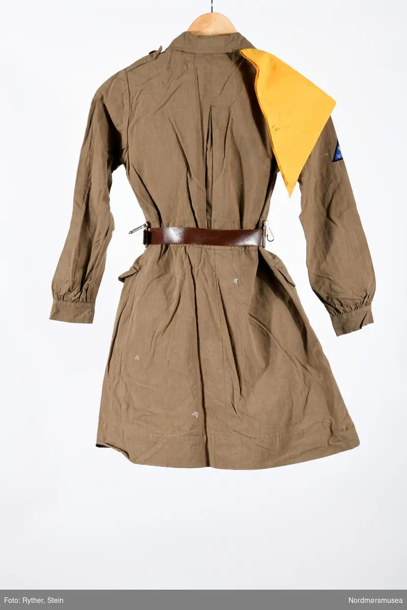 Brun jakkekjole med brunt skinnbelte og gult skjerf til bruk for jentespeiderne i KFUK 1959 (Kristelig ungdomsorganisasjon). Beltet har to metallhemper, sannsynligvis for feste av speiderkniv mm.