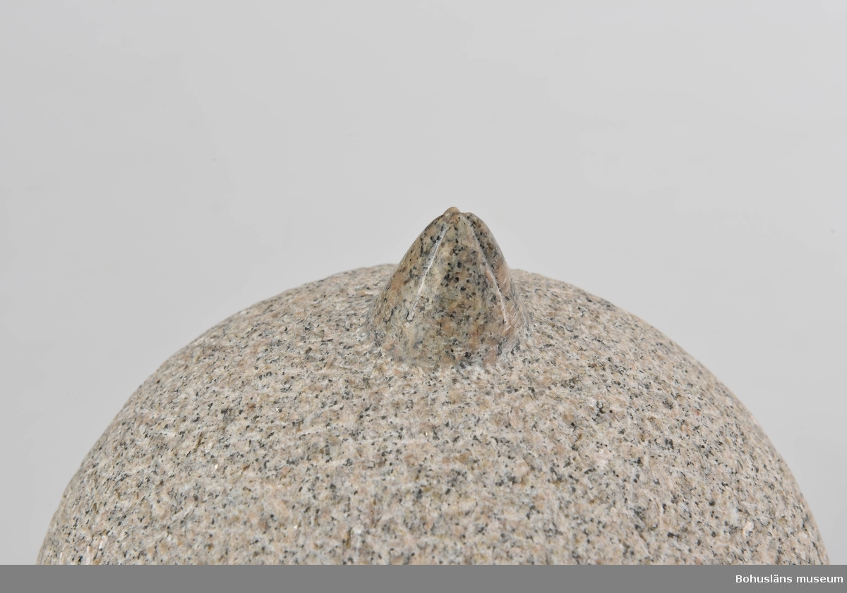 Runt klot av huggen granit med prickhuggen yta. Överst formen av en utsparad och slipad havstulpan. Monterad på en sockel med pyramdformad övre del.
Konstverk till  utmärkelsen "Bohuslän tackar" 1996.