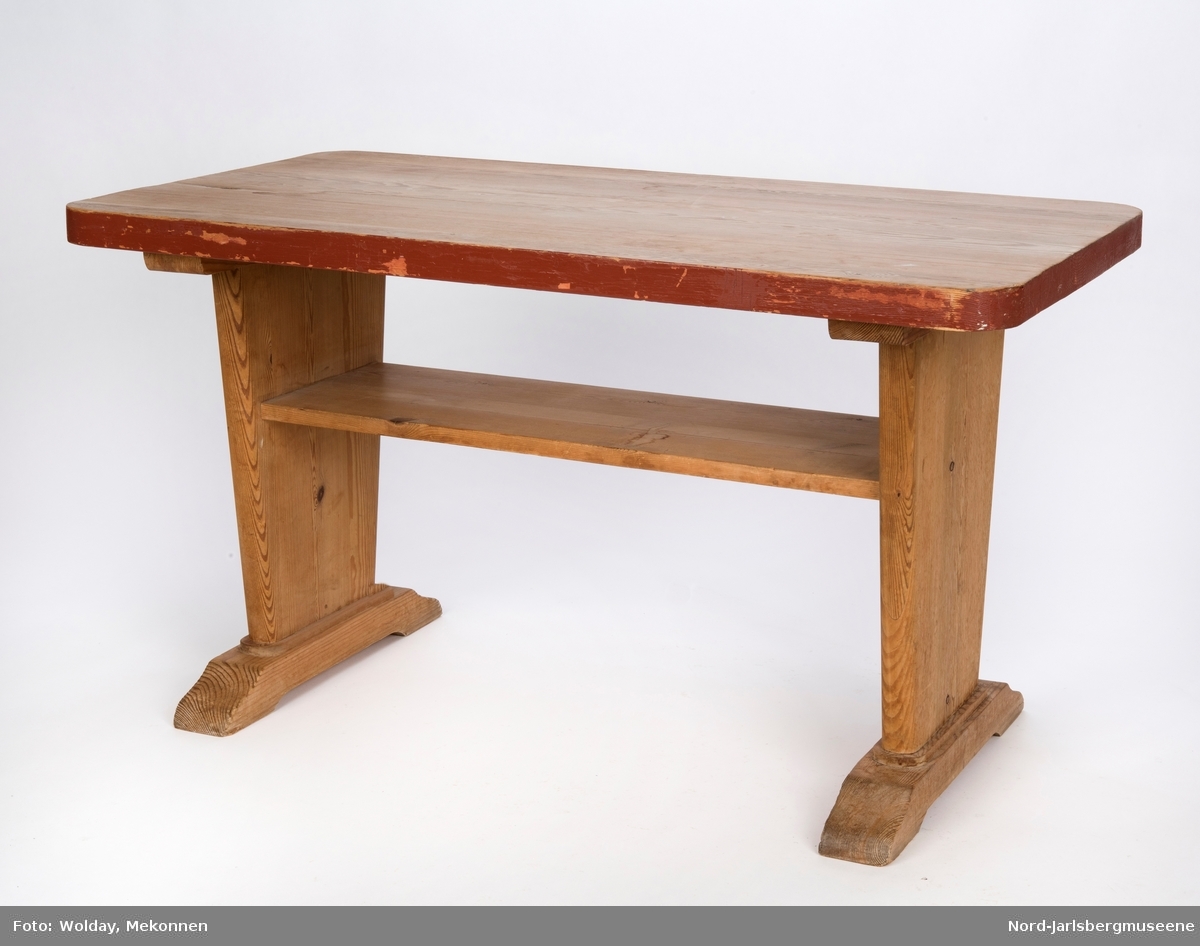 Stuebord med to ben, festet på kortsidene. Tverrgående fotstøtter til bena, bred plate under bordplaten som både stabiliserer og benyttes som hylle. Bordet har en rødtone.