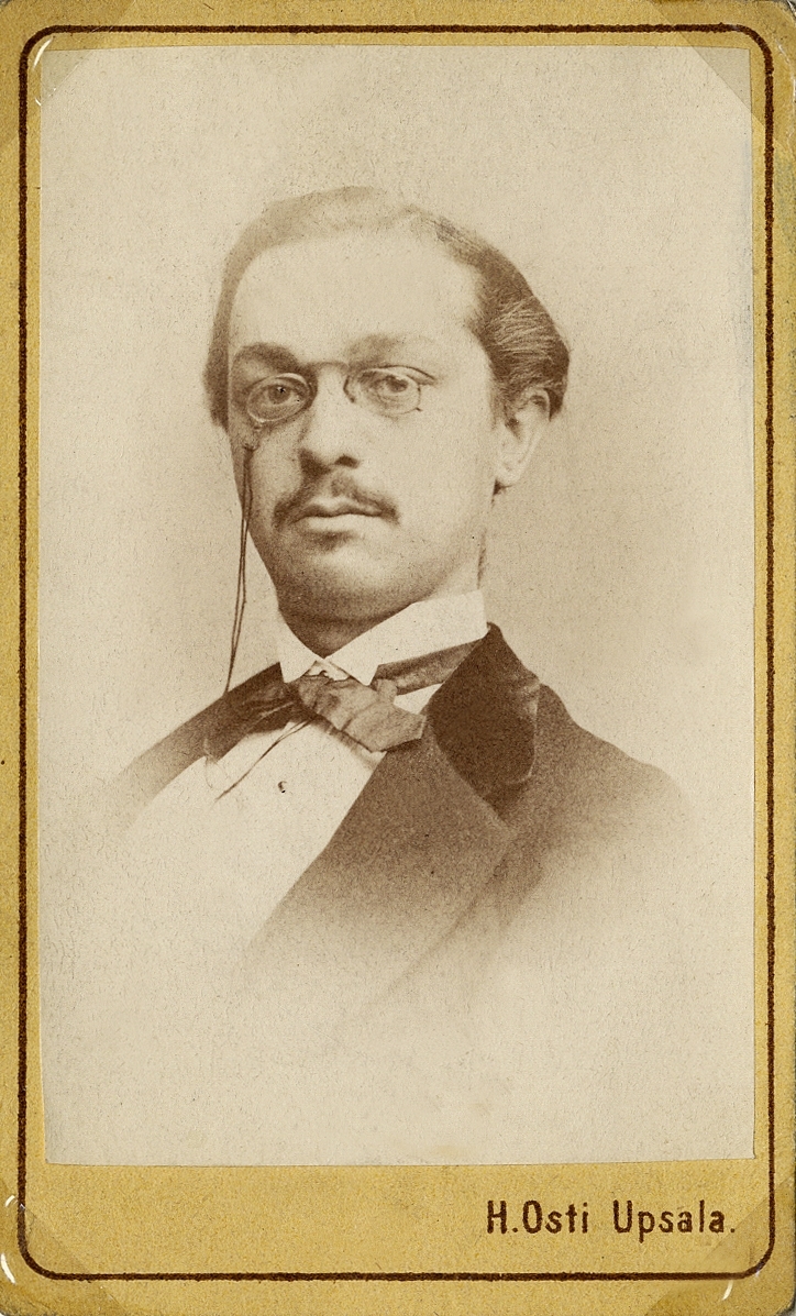 Porträttfoto av en ung man med pincené. Klädd i redingot med sammetskrage, stärkkrage och fluga. 
På baksidan av fotot text: "Claes Crantz 1/12 1871". 
Bröstbild, halvprofil. Ateljéfoto.