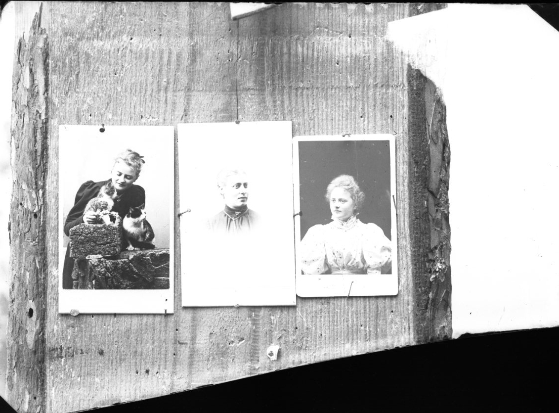 Fotografi av tre små kabinettsfotografier som sitter fästa på en trävägg. Bilderna till vänster och höger visar Ester Grönberg.