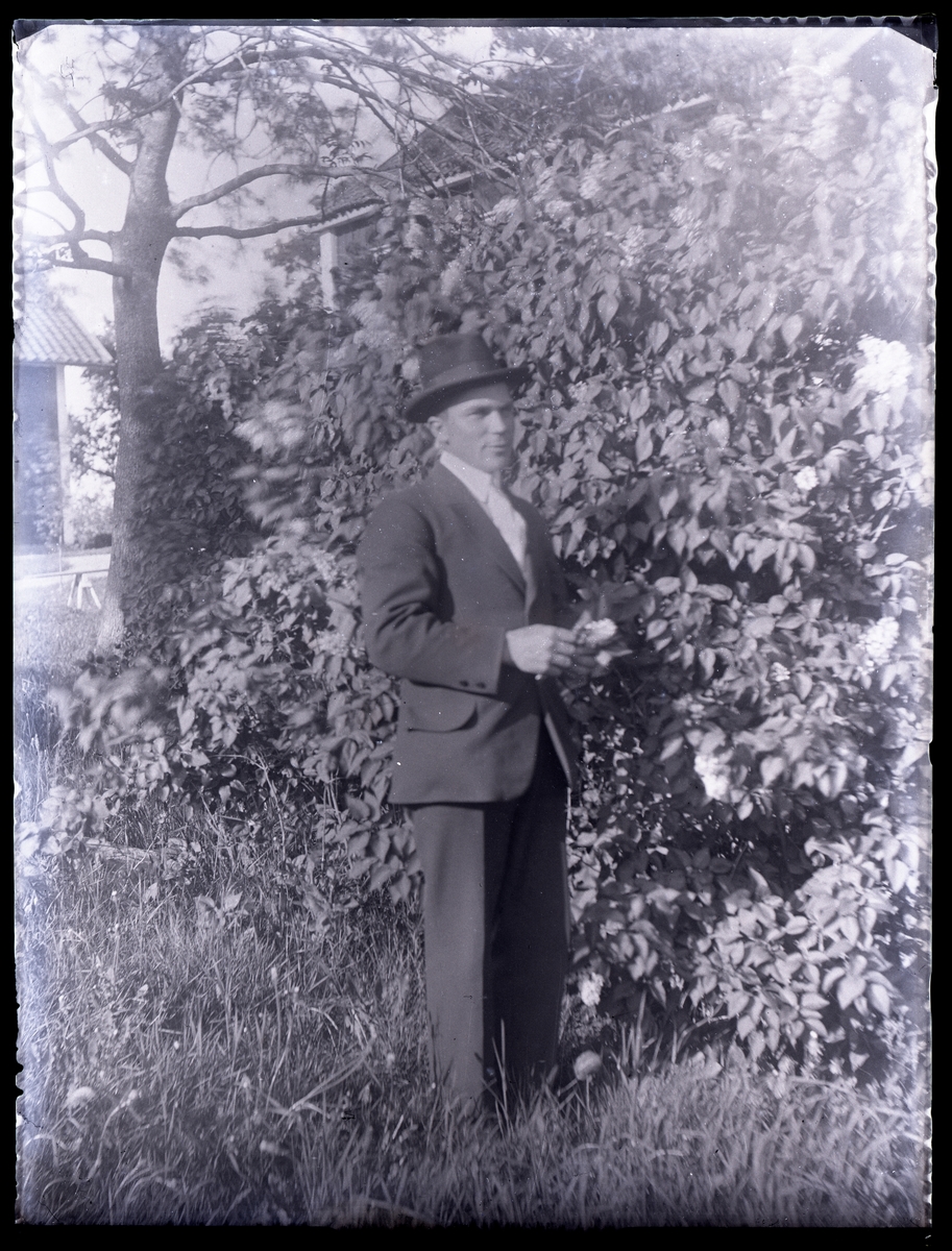 Porträtt av en man, i kostym och hatt, i trädgården.