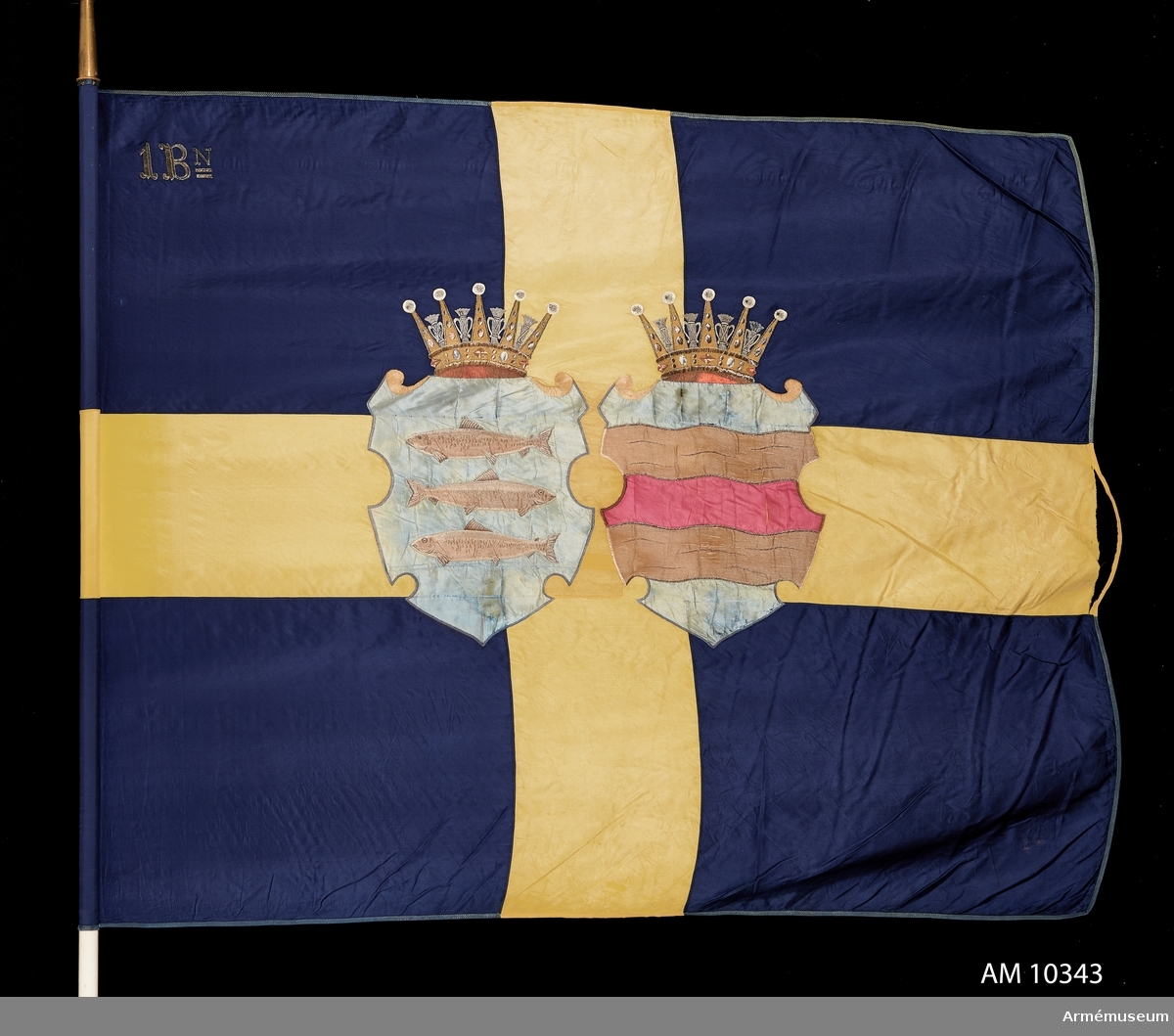 Duk av blått och gult siden med Västernorrlands heraldiska vapen bestående av Ångermanlands och Medelpads vapen i varsin sköld krönta med hertigkronor. I övre stångsidan broderat 1 Bn (första bataljonen).
