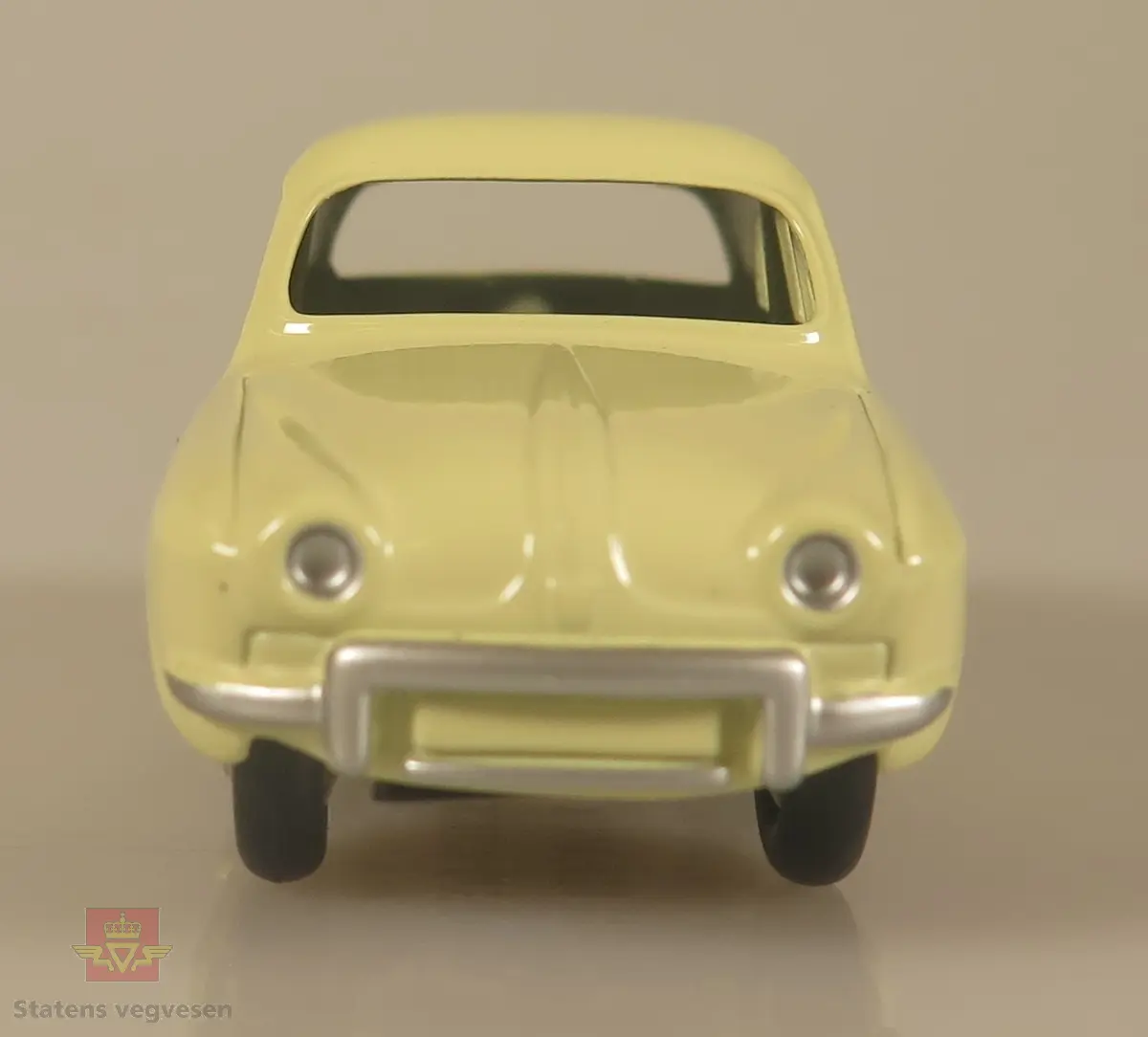 En liten gul modellbil, med kromfarget metallribbe på baksiden av døren.