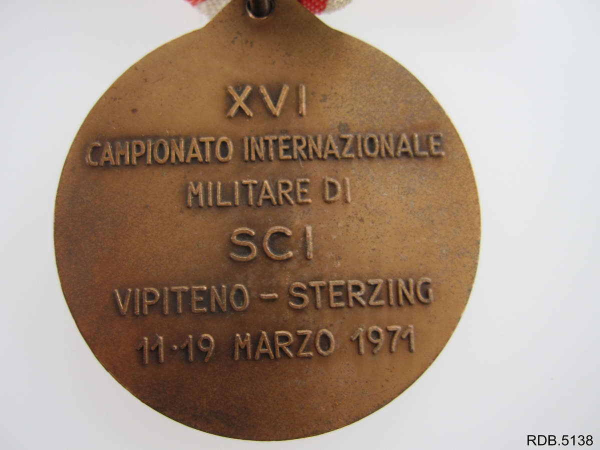 Rund medalje festet til ei sløyfe i rødt, hvitt og grønt. Innskrift på baksiden av medaljen, innskrift og motiv på forsiden av medaljen.