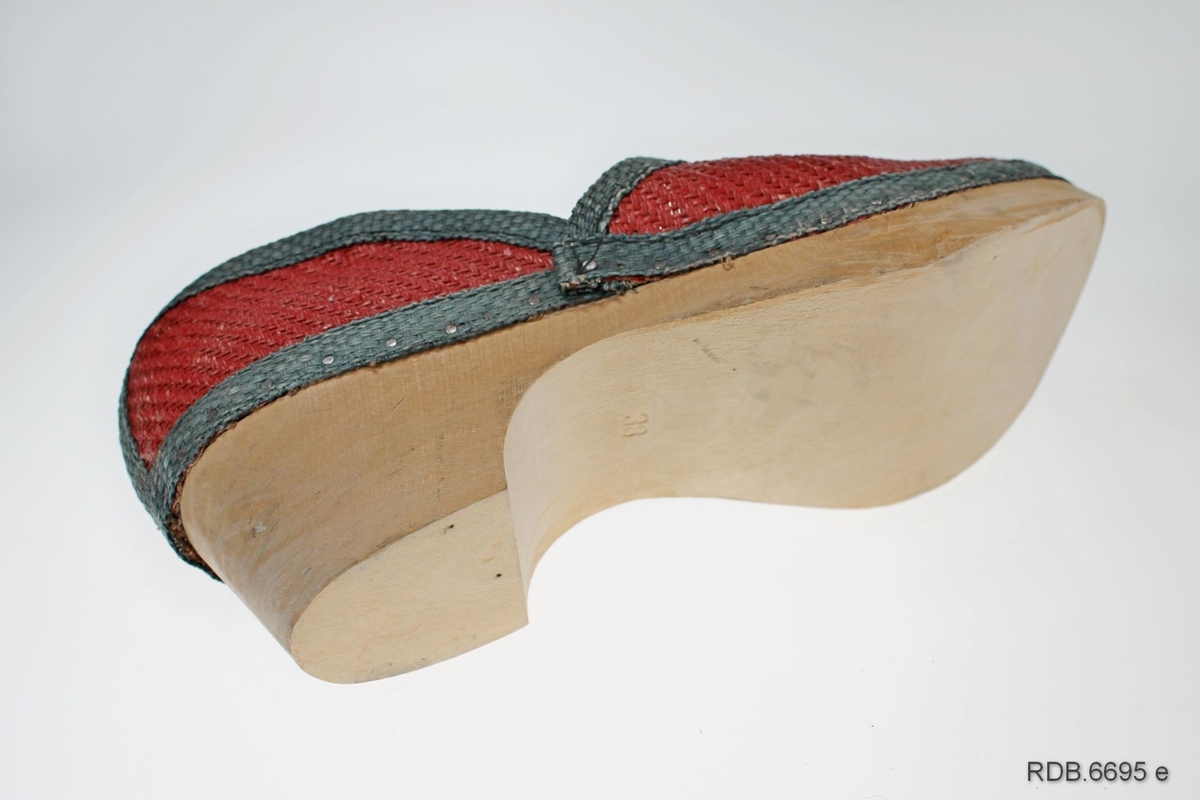 Et par damesko. Skoene er "krigsvare", fra 2. verdenskrig, med overlær av strie og tresåler (trebunner). Skoene er røde med grønne kantebånd. Foran på tåa, på hælen og rundt kanten på skoen er påsydd  forsterkninger av grønt striebånd. Rundt kanten er dette spikret fast til trebunnen. Skoene har kraftige trebunner med litt hæl og er ikke brukt. Venstre sko er str. 37, høgre sko str. 38.