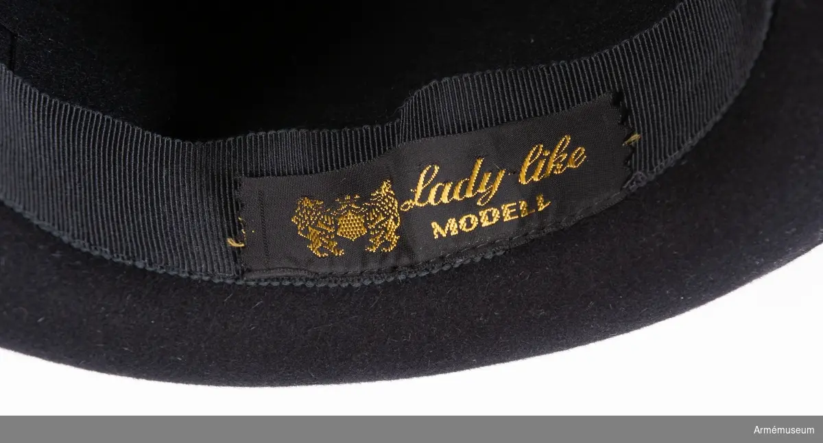 Svart filthatt med svart hattband, rosett samt märke för Svenska Röda Stjärnan. På insidan en märklapp med "Lady like modell".