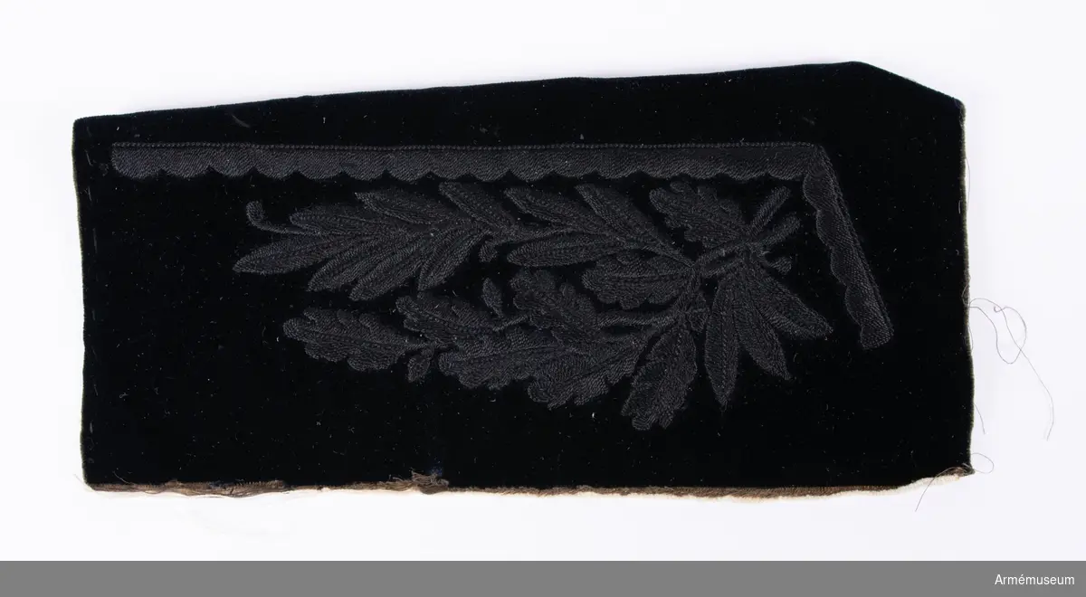 Broderi till krage i svart sammet  med svart broderi i cordonnesilke föreställande två korslagda grenar - en med eklöv och en med lagerblad.