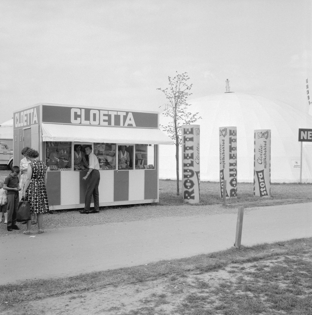 Motiv från utställning NU64 (Norrköpingsutställningen) där en mängd utställare samlades i och kring Himmelstalund sommaren 1964. Ett populärt inslag får vi förmoda att Cloettas kiosk var.