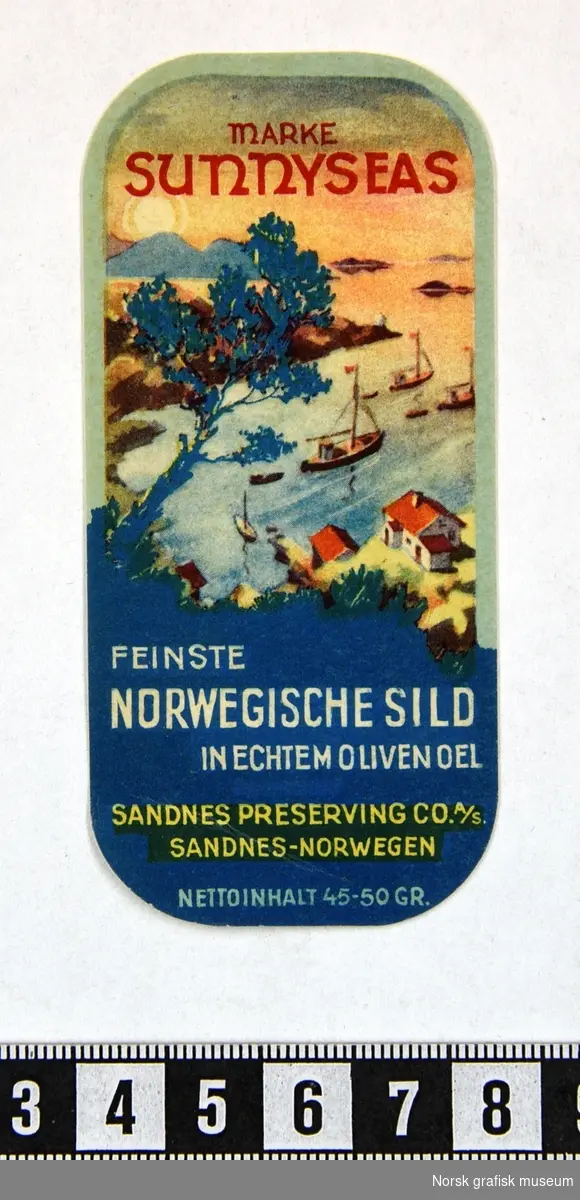 Mindre etikett med et detaljert landskapsmotiv fra en fjord med hvite hus, båter og holmer foran en soloppgang i horisonten. 

"Feinste Norwegische sild in echtem oliven oel" (tysk)
