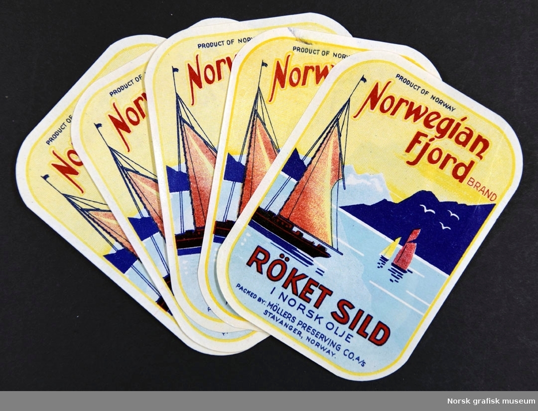 Etiketter med en illustrasjon av seilbåter på sjøen med fjell i bakgrunn. 

"Röket sild i norsk olje"