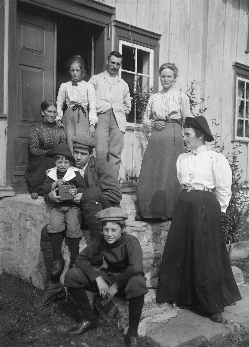Gruppeportrett av en familie som står på trappa foran et hus. Familien Aston/ Eikrem?