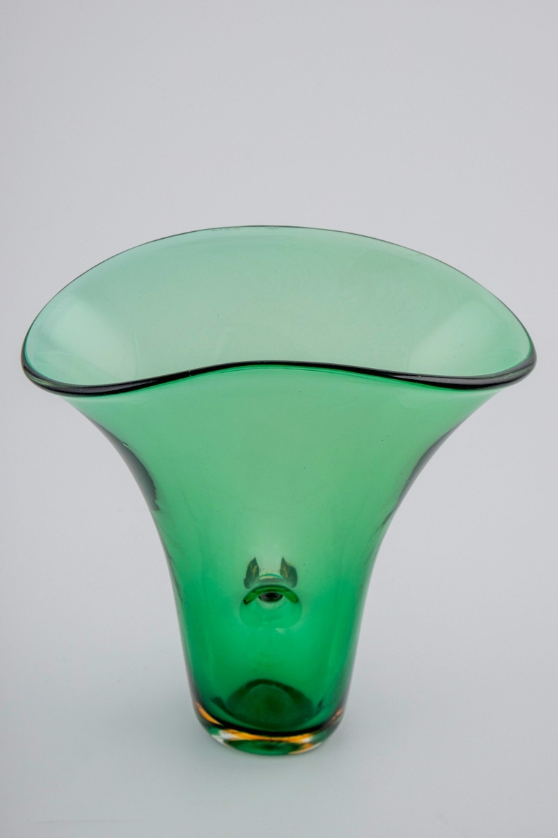 Grønnfarget vase i gjennomskinnelig glass. Vasen hviler på en ovalformet bunn, som er utført i gulbrunt og klart glass i overfangsteknikk. Fra den smale bunnen reiser vasens vegger seg i en bred vifteform, hvor langsidene er forbundet med et gjennomgående hull i midten. Ujevn ovalformet munningsrand.