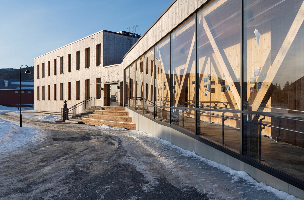 Administrasjons- og undervisningsbygningen som ble reist ved Høgskolen i Innlandets studiested Evenstad i Stor-Elvdal i 2016. Huset er reist med massivtre i de viktigste bærekonstruksjonene. Det er isolert med trefiber og har ytterkledning av malmfuru, og en del av glassflatene er av gjenbruksmateriale fra Statsbyggs hovedkontor i «Byporten» i Oslo. Byggeprosjektet var preget av ambisjoner om å reise et hus som gjennom sitt livsløp skulle bli minst mulig miljøbelastende, samtidig som det skulle speile treets gode egenskaper i slike sammenhenger. Denne tankegangen er også noe av bakgrunnen for at varme og elektrisk energi i denne bygningen produseres av flis fra den regionen huset står i.

Statsbygg var byggherre da dette huset ble reist etter tegninger fra Ola Roald Arkitektur. Hovedentreprenør var Kongsvinger-firmaet Ø. M. Fjeld. Bygningen fikk «Innlandets trepris 2017» og ble også anerkjent som «Første ZEB-COM-bygg i Norge».

Utdanningsinstitusjonen på Evenstad ble etablert som skogskole i 1912. Bakgrunnen for denne skoleetableringa var at den forrige eieren av Evenstad, Anne Olsadatter Evenstad (1830-1909), hadde opprettet et stort legat med sikte på at unge østerdøler skulle kunne skaffe seg praktisk og teoretisk utdanning i skogbruk. Sjøl hadde Anne, som var oppvokst på et mindre gardsbruk i Stor-Elvdal, kommet til Evenstad som tjenestejente. Hun ble forlovet med odelsgutten på garden, Ole Evenstad IV (1827-1859). Anne ble gravid, og det ble planlagt bryllup. Forloveden døde imidlertid før bryllupet, og kort tid deretter døde også han som skulle blitt svigerfar. Ole Olsen Evenstad III (1798-1859) hadde imidlertid testamentert eiendommen til Anne og hennes ufødte barn. Dermed fikk hun ansvaret for å forvalte verdiene videre med sikte på at sønnen hennes skulle føre slektstradisjonen videre. Ole Olsen Evenstad V (1859-1891) studerte skogbruk ved tyske forstakademier (Aschaffenburg og München), og viste seg som en samfunnsengasjert og evnerik mann, men døde ung. Dermed ble Anne på sine eldre dager sittende aleine med eiendommen, som hadde cirka 400 dekar dyrket mark og 26 500 dekar skog. Dette var bakgrunnen for den nevnte legattransaksjonen. Etter Anne Evenstads død kjøpte Stor-Elvdal kommune garden og stilte den til disposisjon for Hedemarkens amtskommune (Hedmark fylke), slik at de kunne realisere idéen om å etablere en skogskole. På dette fotografiet skimter vi Anne Evenstads byste på en granittsokkel ved trappa mot hovedinngangen. 

I 1989 ble Evenstad skogskole innlemmet i Hedmark distriktshøgskole. I denne fasen ble studietilbudet utvidet med andre utmarksfag, og det ble satset stort på viltforskning. Det utvidete fagspekteret bidro nok til at Evenstad overlevde i en periode da flere av de andre skogskolene i Norge ble avviklet. I tillegg til skogbruk og utmarksforvaltning har Evenstad også anvendt økologi og jakt-, fiske- og naturveiledning på studieplanen. Skolen tilbyr også kortere kurs naturoppsyn og bruk av GIS-metodikk i skog- og utmarksnæringene. Opprinnelig foregikk teoriundervisningen i 2. etasje i den digre hovedbygningen Anne Evenstad hadde fått ferdig i slutten av 1860-åra (grunnflata var på drøyt 350 kvadratmeter). Dette huset ble dessverre herjet av brann en stormfull vinterdag i 1987. Et nytt undervisningsbygg ble ferdigstilt i 1990. Et stadig bredere undervisningstilbud - og dermed flere ansatte og studenter - var bakgrunnen for at bygningen på dette fotografiet ble reist i 2016.