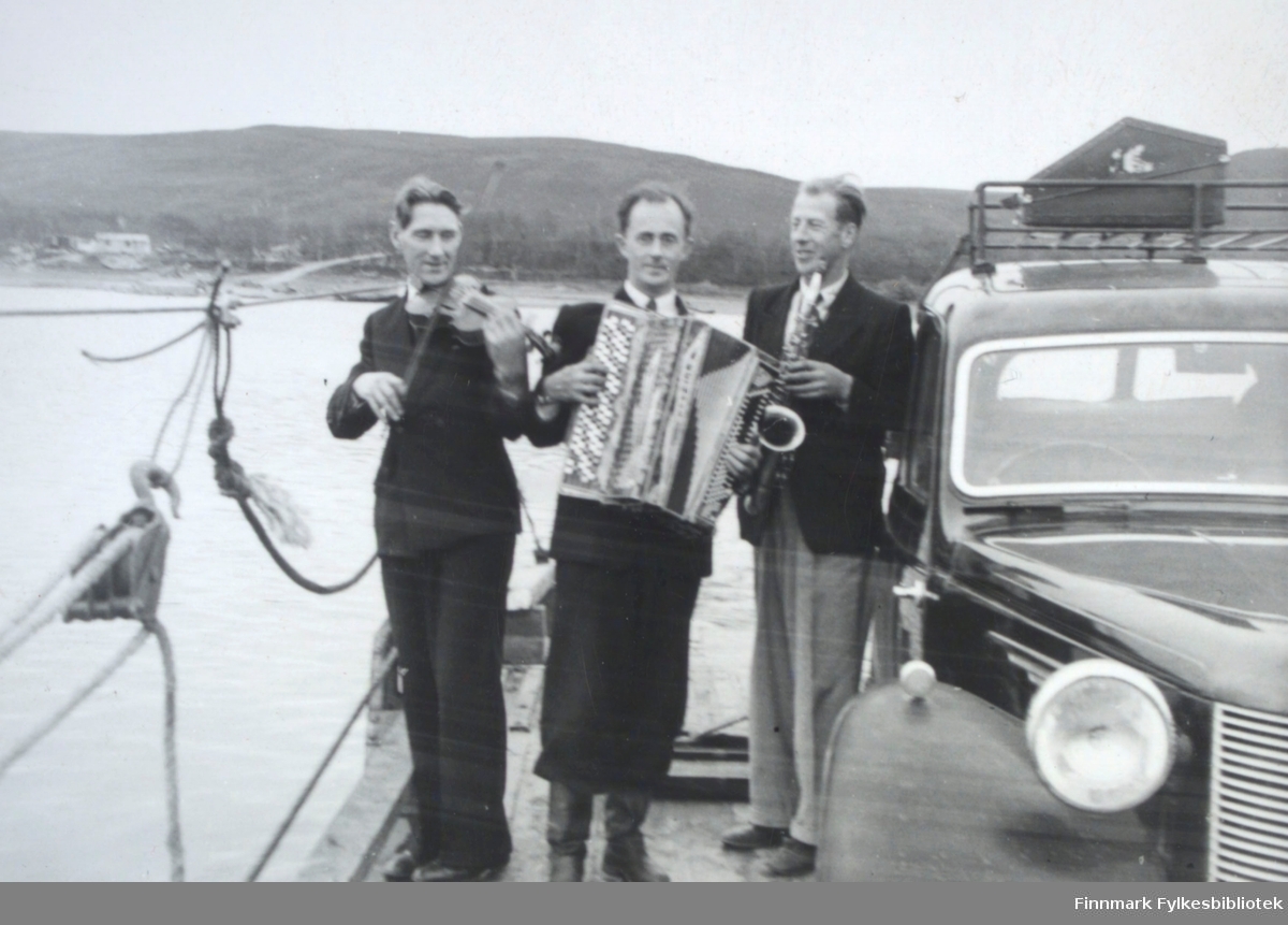 Fra venstre: Ole Johnsen (fiolin), Ivar Sælø (trekkspill) og Edmund Jankila (saxofon). Et sted langs Tanaelva med ferge, muligens i Seida, på 1950-tallet. Ivar Sæløs bil Austin A10 til høyre.