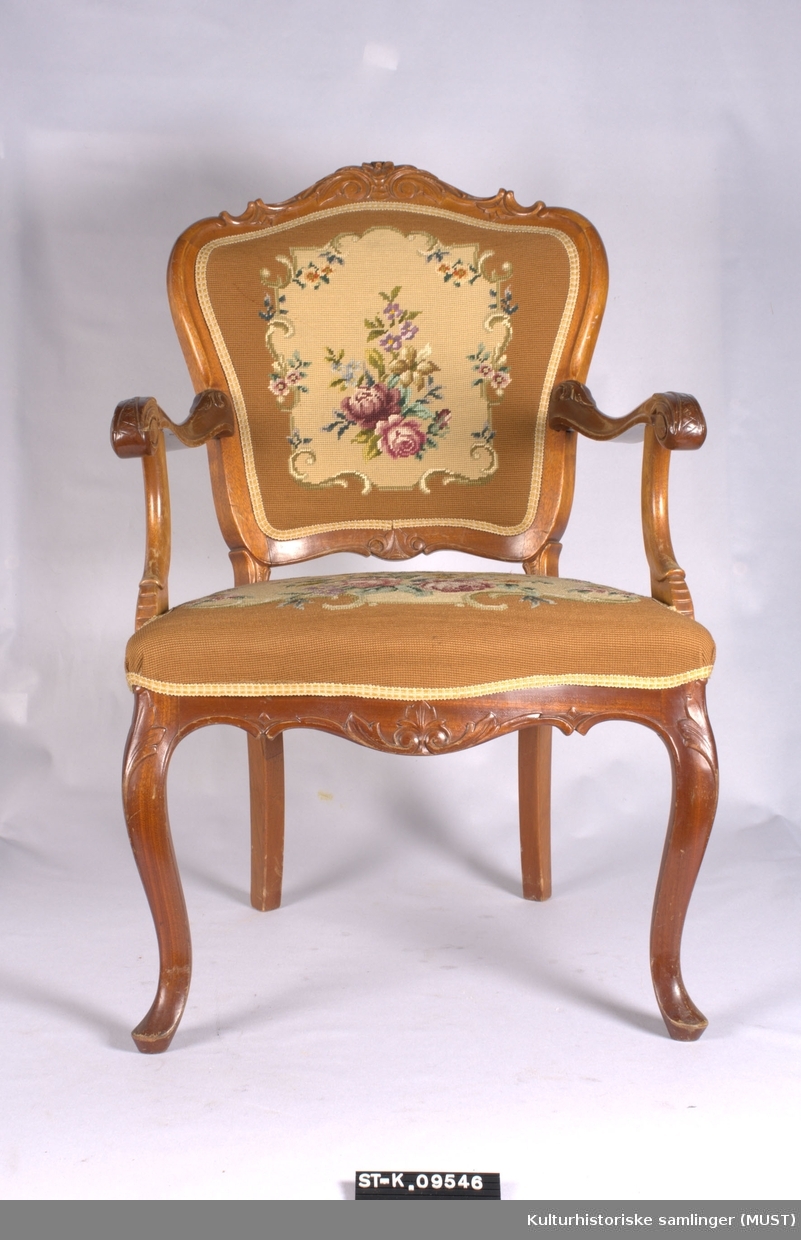 Armstol av mahogny med brodert trekk på sete og rygg. Svugne armelener, og frambein. Utskåret med blomster og akantus.
