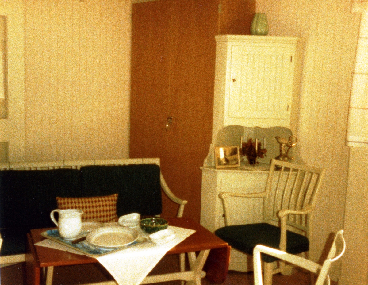 Brattåsgården vid invigningen år 1986. Utställning av föremål från gamla Brattåshemmet, gjord av Kållereds Hembygdsgille. Delar av föremålen finns nu på Mölndals stadsmuseum. Här ses hörnskåp, soffa och två stolar (allt i vitt) samt ett avlångt bord av trä.