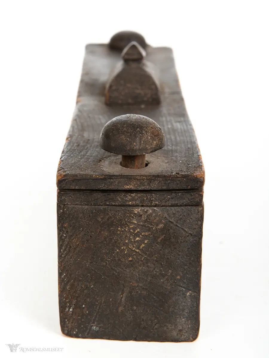 Rektangulær stokkeske hulet ut av et stykke tre. Dreielokk som har en sperreplate som dreier om en tapp og låses mot en låsekloss som holder hovedlokket låst mot en tapp på motsatt side.