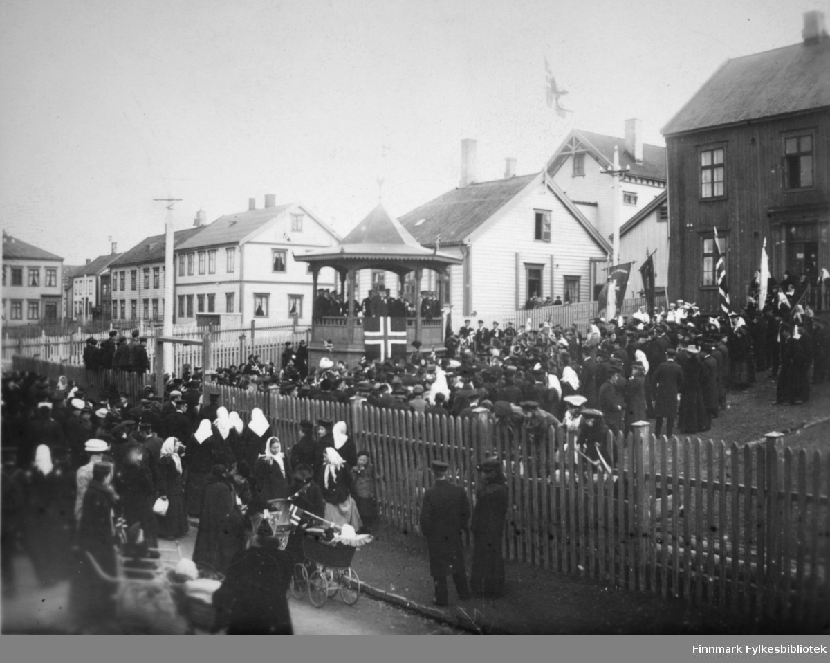 Musikkpaviljong i Vadsø muligens i begynnelsen av 1900-tallet 17. mai feiring med mye folk. Mange kvinner med hvite skjerf.